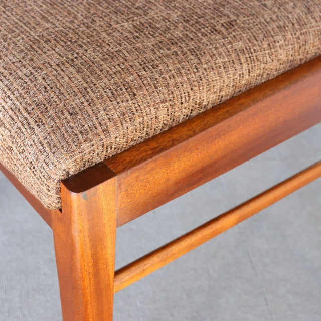 Mid-century British McIntosh teak dining chair corner showing rich wood grain and textured brown fabric seat.