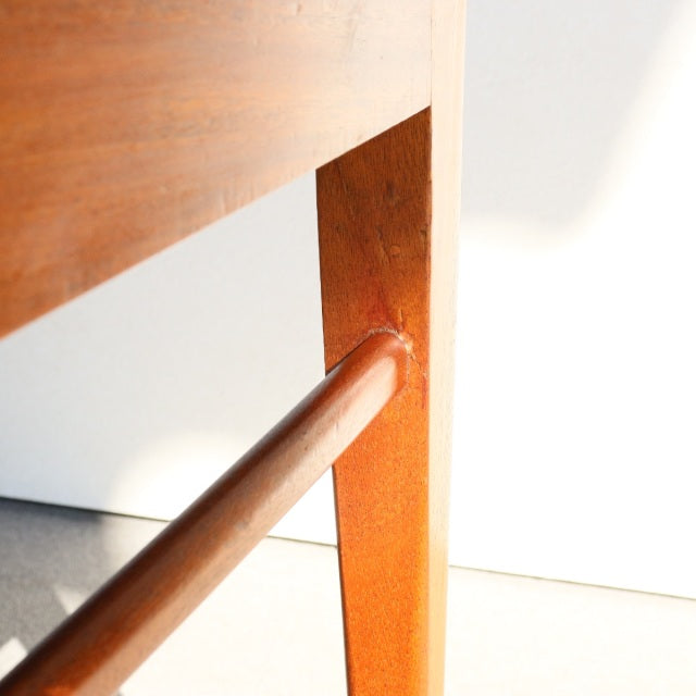Close-up of mid-century British McIntosh teak dining chair leg showcasing rich wood grain and smooth finish.
