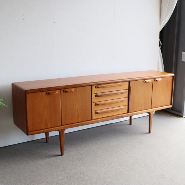 Mid-century British vintage teak sideboard by Younger with rich wood grain, four splayed legs, cabinet doors, and central.