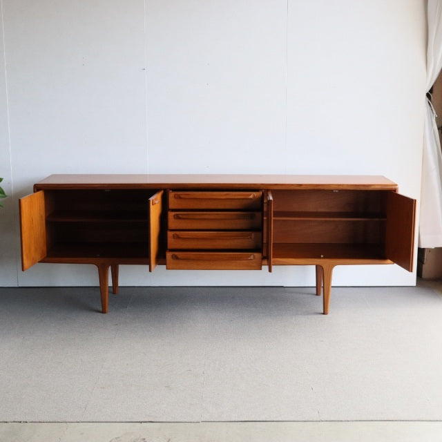 Mid-century British vintage teak sideboard by Younger with rich wood grain, four tapered legs, two open side cabinets, and.