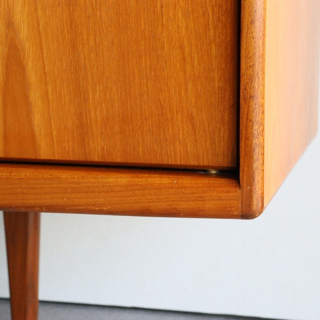 Close-up of vintage British mid-century teak sideboard corner showing smooth wood grain and tapered leg details.