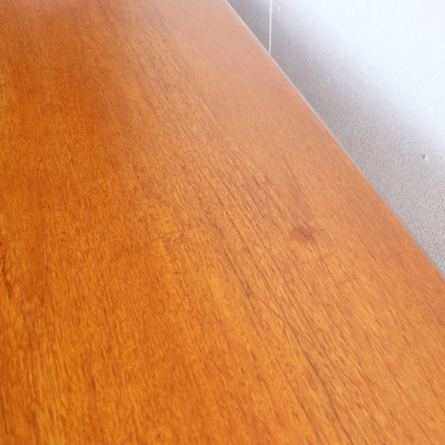 Close-up of vintage teak sideboard surface showing warm honey wood grain from British mid-century design by Younger, smooth.