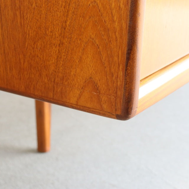 Close-up of mid-century British vintage teak sideboard corner showing smooth wood grain and tapered leg detail.