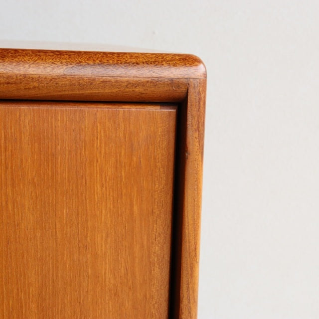 Close-up of vintage British mid-century teak sideboard corner showing rich wood grain and smooth rounded edges.