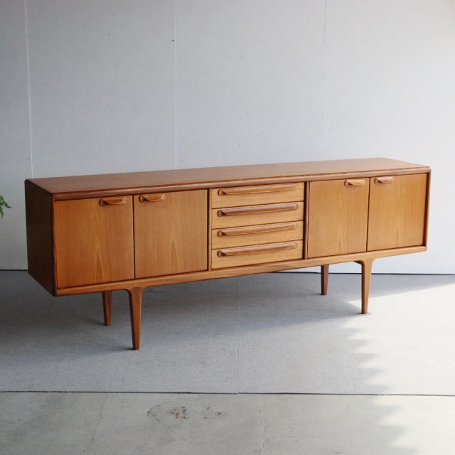 Mid-century British vintage teak sideboard by Younger with smooth wood grain, tapered legs, and four central drawers flanked .