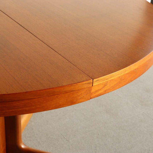 Round vintage teak dining table with smooth grain, mid-century British-Denmark design, sturdy rounded legs.