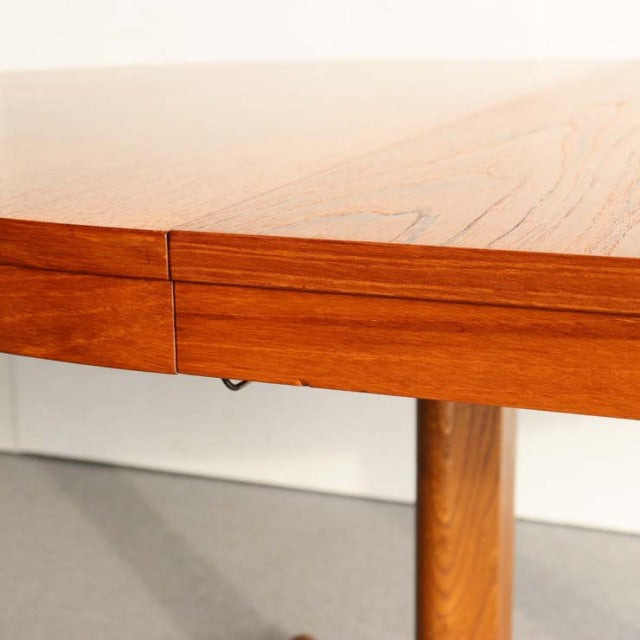 Round mid-century dining table by Edward Valentinsen in warm teak with visible wood grain and slender cylindrical legs,.