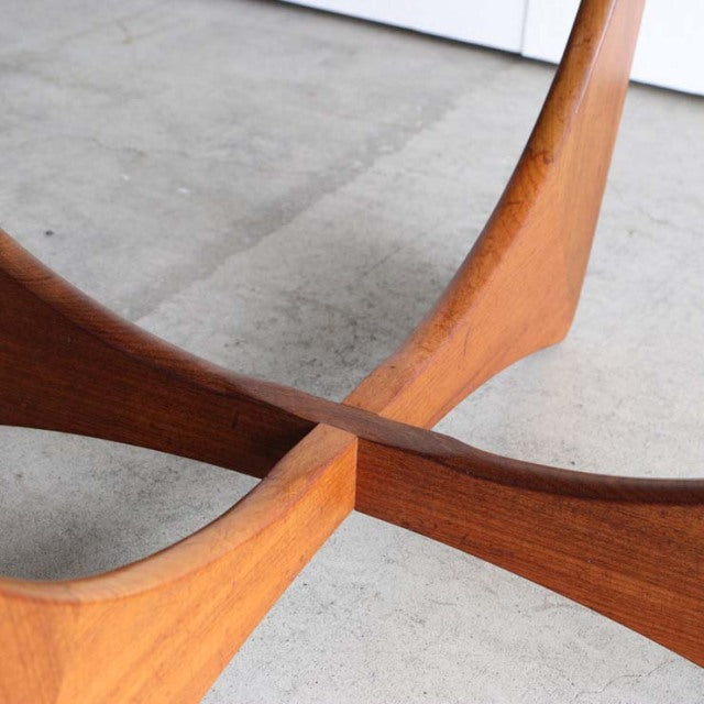 Mid-century British teak coffee table base with smooth rounded legs crossing in the center, showcasing rich wood grain and.