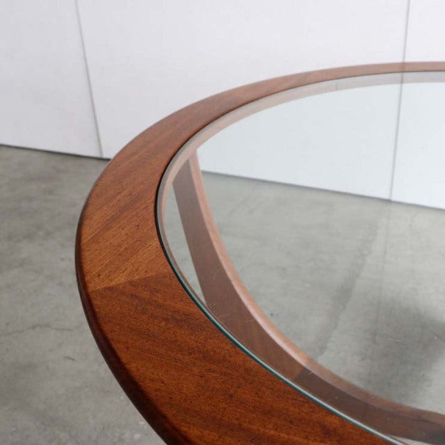 Vintage British mid-century G-Plan coffee table with round teak frame and clear glass top showing wood grain and angled legs.