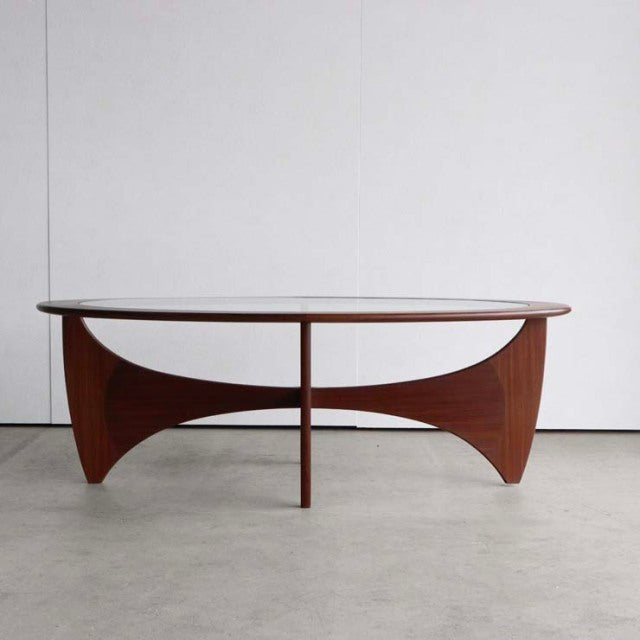 Oval mid-century British G-Plan coffee table with clear glass top and curved vintage teak legs showing rich wood grain.