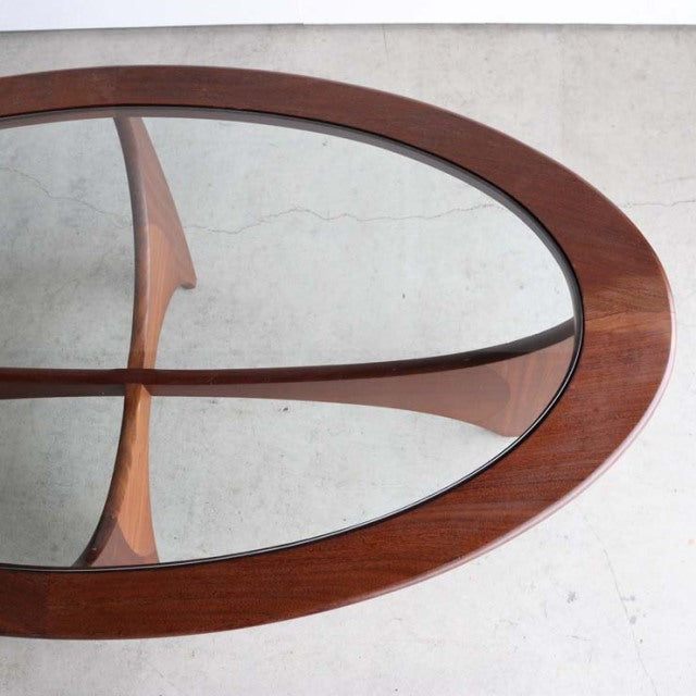 Oval mid-century British vintage teak coffee table with glass top and sculpted wooden legs, showcasing rich wood grain and.