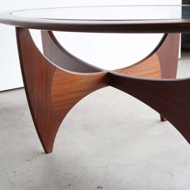 Mid-century British G-Plan teak coffee table with oval glass top and sculptural curved wood base showing rich wood grain.