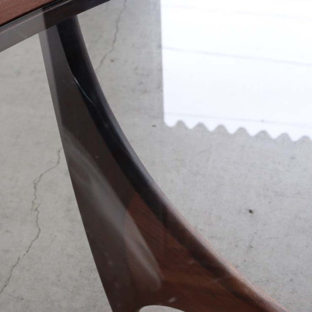 Close-up of vintage British mid-century teak coffee table leg with rich wood grain under oval glass top.