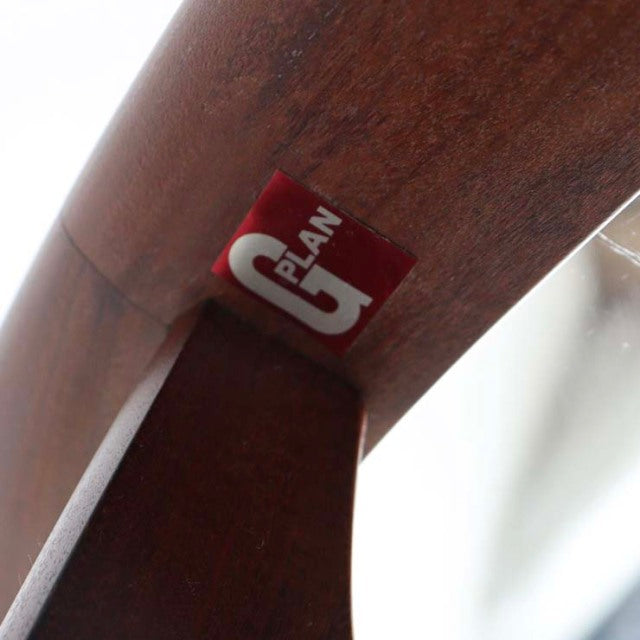 Close-up of vintage British G-Plan teak coffee table leg with rich wood grain and red brand label under glass oval top.