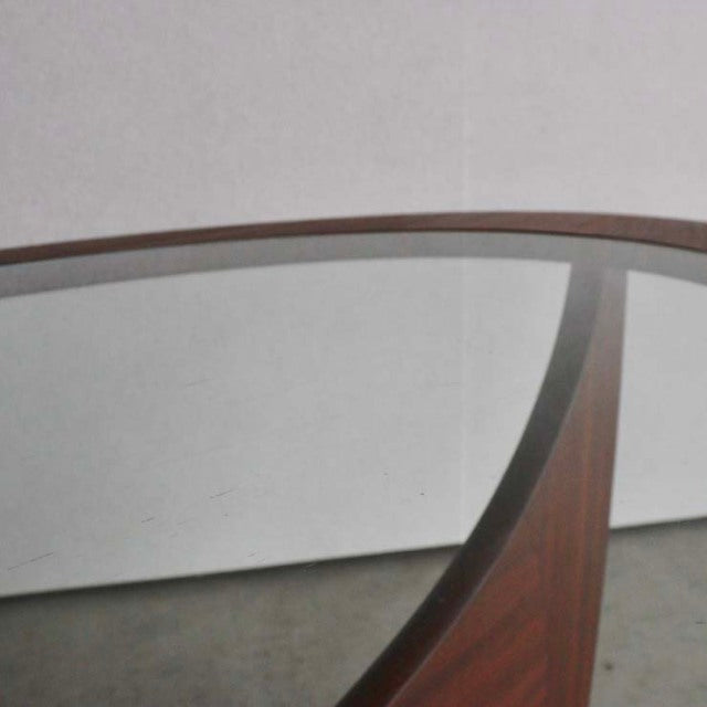 Mid-century British vintage teak coffee table with oval glass top and curved wooden base showcasing rich wood grain.