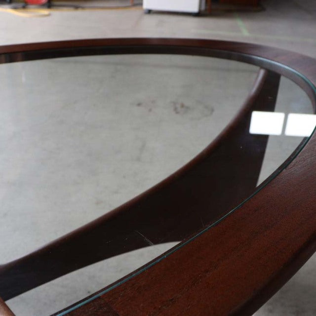 Oval mid-century British vintage G-Plan teak coffee table with clear glass top and smooth wood grain edges.