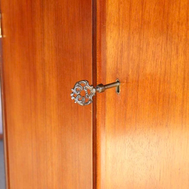 Mid-century British vintage teak cabinet door with ornate metal key and warm wood grain detailing.