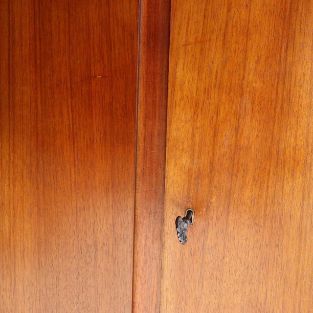 Close-up of vintage British mid-century teak cabinet door showing rich wood grain and brass keyhole detail.