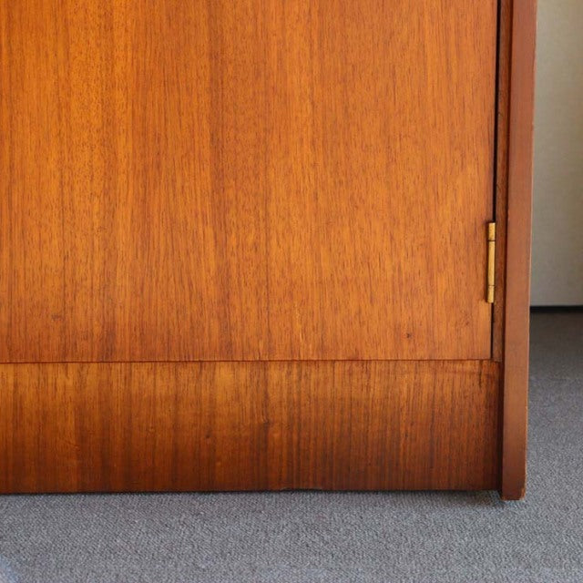 Close-up of vintage mid-century teak cabinet door showing rich wood grain and brass hinge, British design influence.