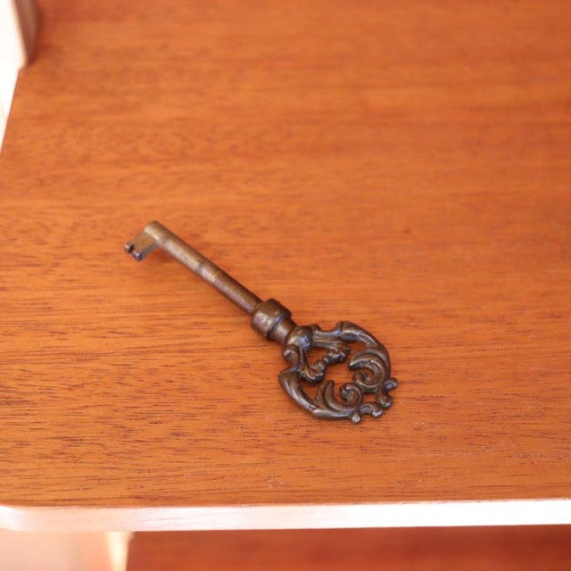 Ornate vintage brass key resting on smooth teak wood surface showcasing fine grain and warm mid-century Danish craftsmanship .