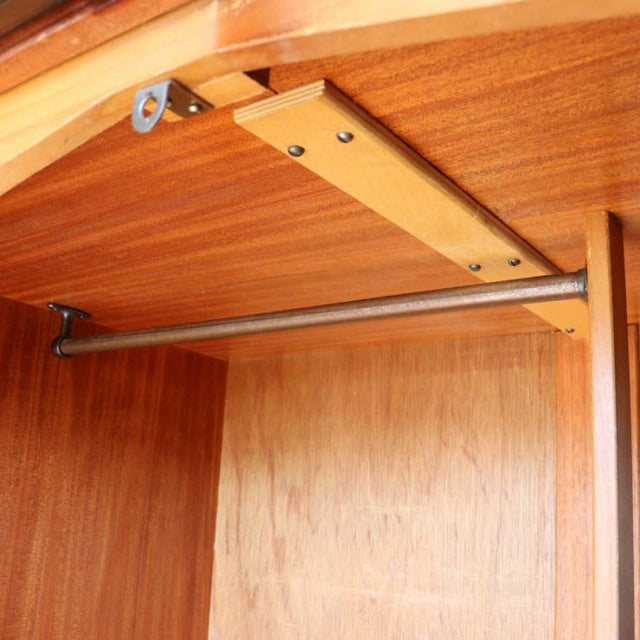 Mid-century British vintage teak wardrobe interior with smooth wood grain, sturdy metal hanging rod, and clean joinery.