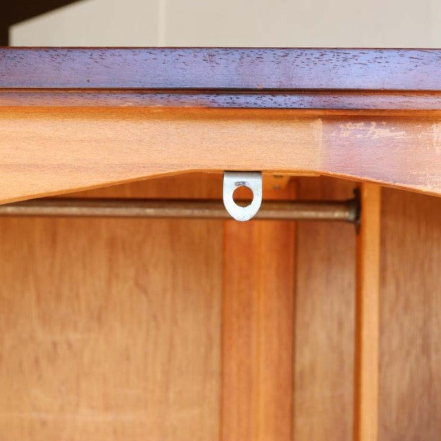 Close-up of vintage teak wood grain and curved British mid-century cabinet frame with metal hanging bracket visible inside.