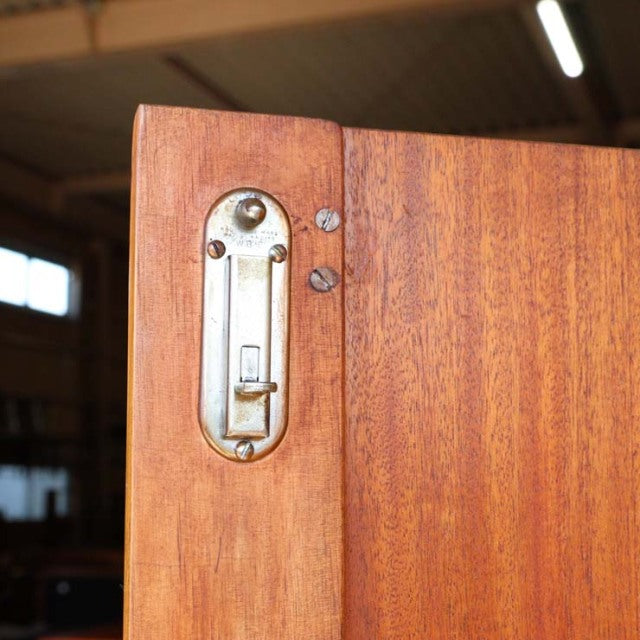 Close-up of vintage mid-century teak cabinet door corner showing smooth wood grain and brass British lock plate by William.