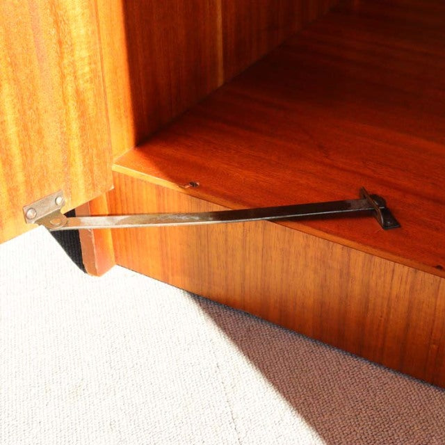 Mid-century British teak cabinet corner showing smooth wood grain and metal support hinge from William Laurence vintage.