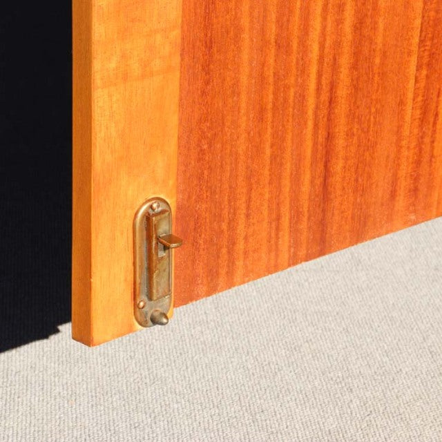 Close-up of vintage teak cabinet door edge with brass latch, showcasing fine wood grain and mid-century British craftsmanship.