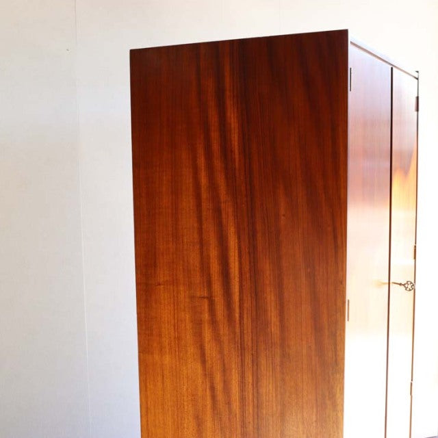 Vintage teak wardrobe with rich wood grain, mid-century British design, clean rectangular form, subtle brass hardware, and.