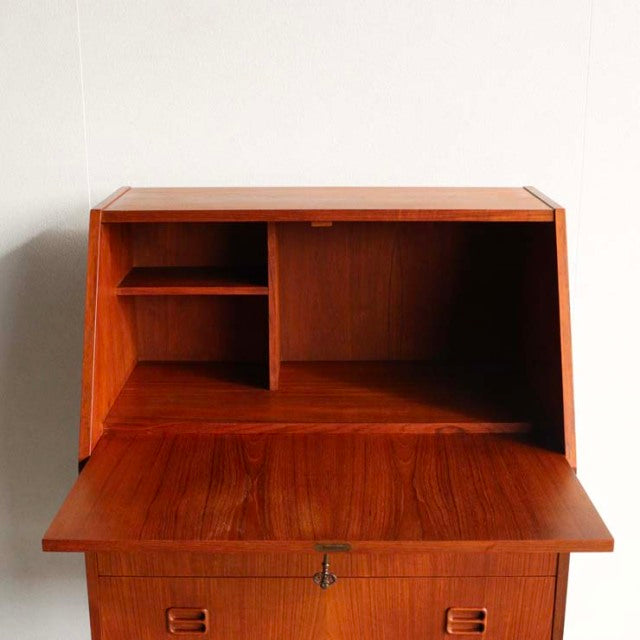 Vintage mid-century Danish teak bureau by Gunnar Nielsen Tibergaard with fold-down writing surface, visible wood grain, and.