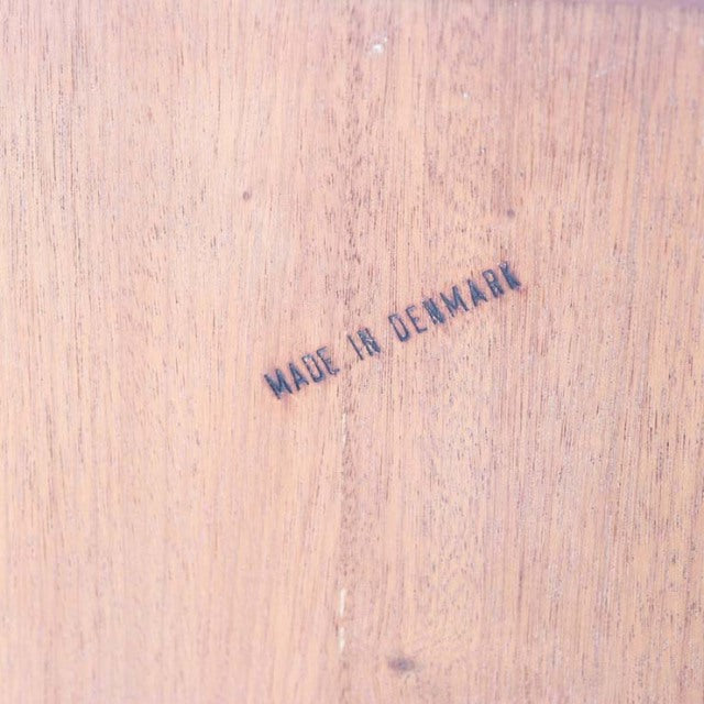 Close-up of teak wood grain with "Made in Denmark" stamped, vintage mid-century British-Danish furniture mark.