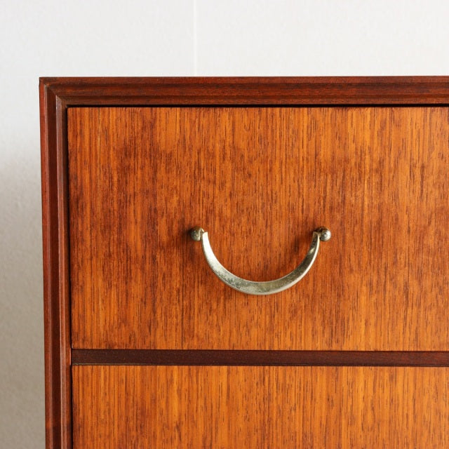 Mid-century British vintage teak chest drawer with curved brass handle and warm wood grain detailing.