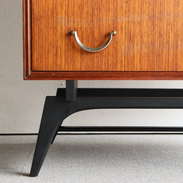 Mid-century British vintage teak chest corner with warm wood grain and curved brass handle on black angled leg frame from.