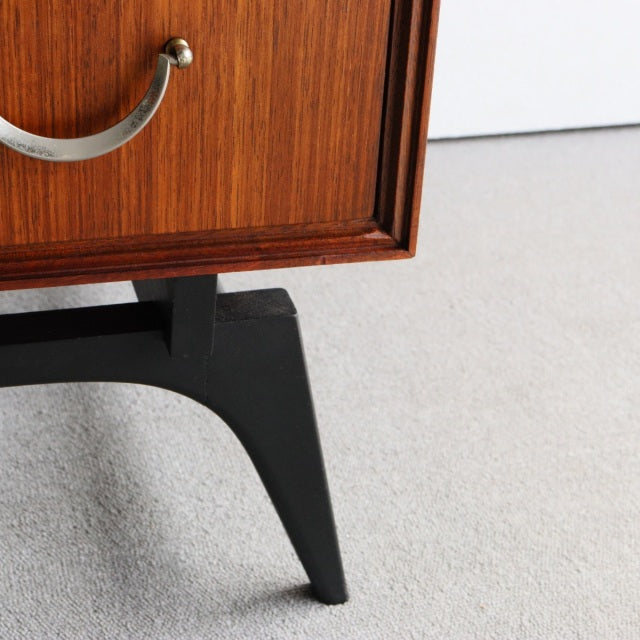 Mid-century British teak chest corner with rich wood grain and sleek black angled leg detail.
