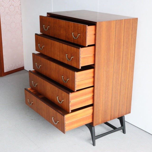 Mid-century British teak 5-drawer chest by Meredew with rich wood grain, brass handles, and black angled legs, vintage.