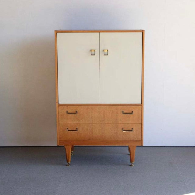 Vintage G-Plan teak mid-century cabinet with cream doors, two drawers, brass handles, and tapered legs.