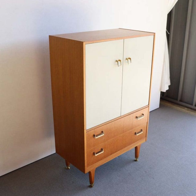 Vintage British G-Plan teak tallboy cabinet with white doors, wood grain, and tapered legs.