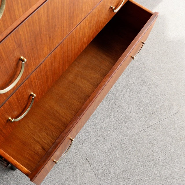 Mid-century teak five-drawer chest by Meredew with brass handles, visible wood grain, and tapered legs, British vintage.