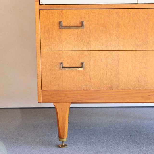 Vintage British mid-century teak G-Plan cabinet showing rich wood grain, tapered legs with brass caps, and metal handles.