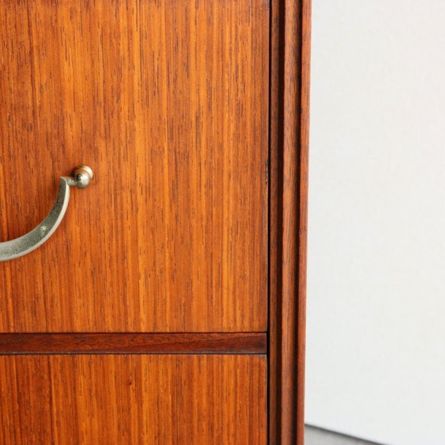 Close-up of vintage British mid-century teak chest drawer showing rich wood grain and curved brass handle.