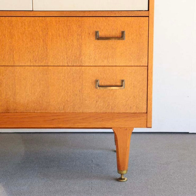 Mid-century British G-Plan teak cabinet showing rich wood grain, brass handles, and tapered leg with brass caster.
