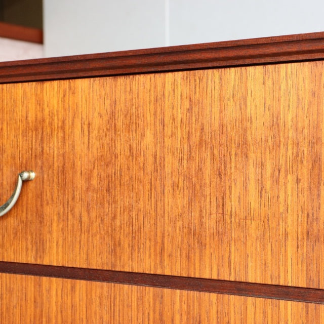 Mid-century British teak five-drawer chest by Meredew with wood grain and brass handles.
