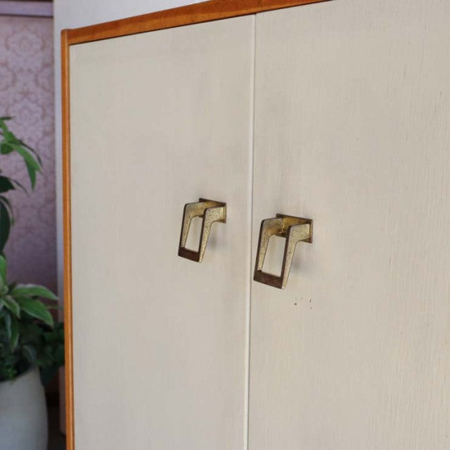 Vintage British mid-century teak cabinet with clean vertical grain, square brass handles, and sleek frame edges.