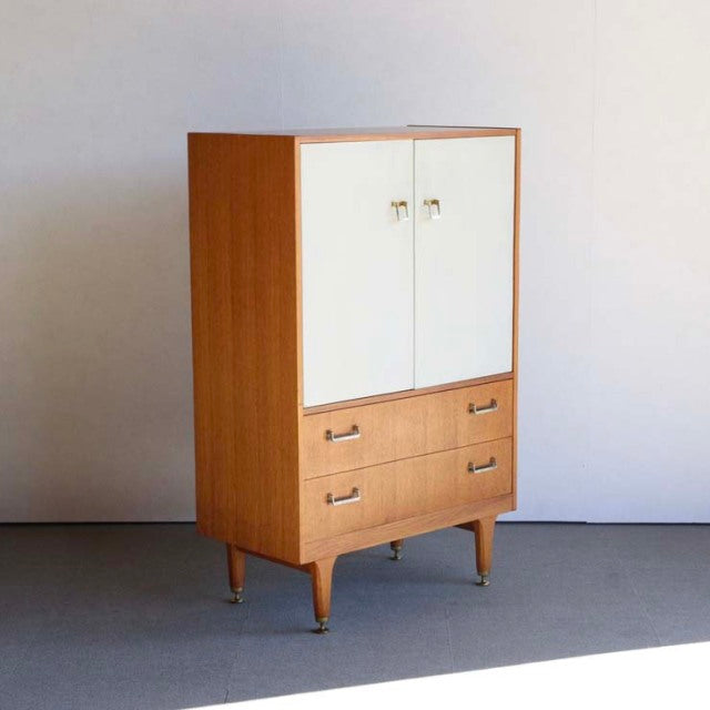 Mid-century British G-PLAN teak cabinet with white doors, four drawers, and tapered legs.
