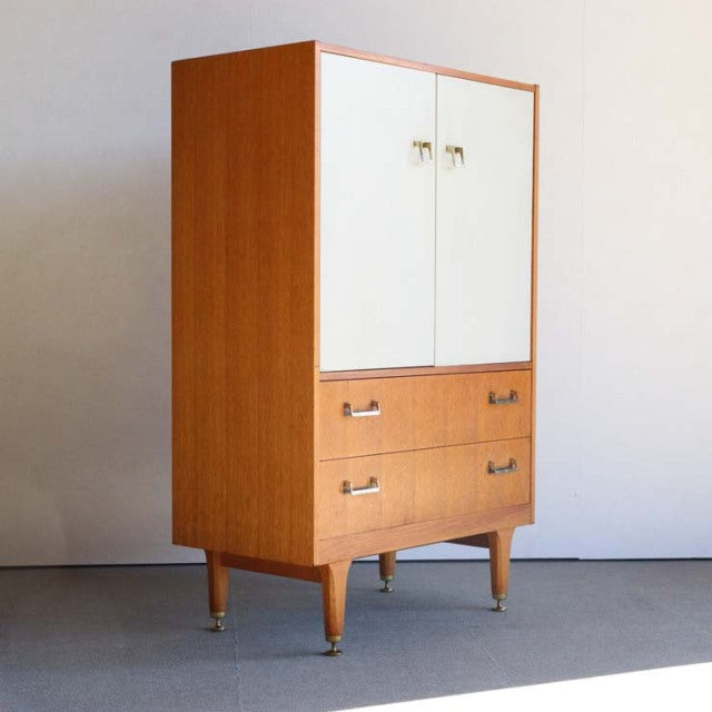Mid-century vintage British G-Plan teak tallboy cabinet with white doors, wood grain, and tapered legs.
