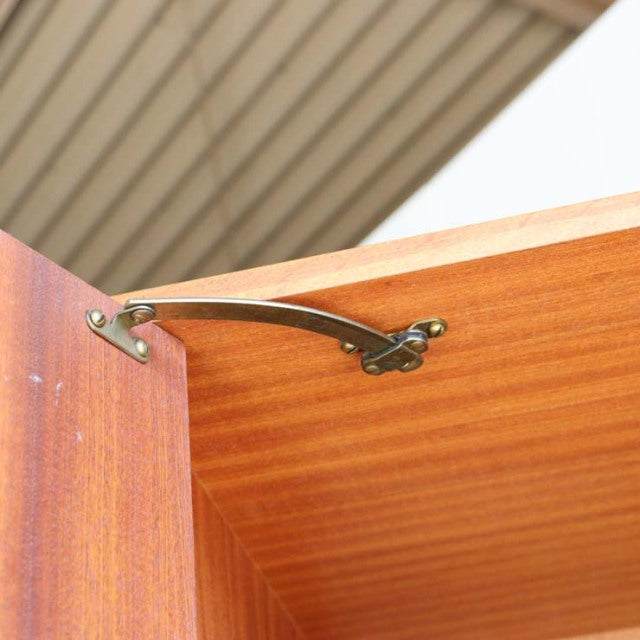 Close-up of vintage G-PLAN teak cabinet door hinge showcasing smooth wood grain and brass hardware detail from mid-century.