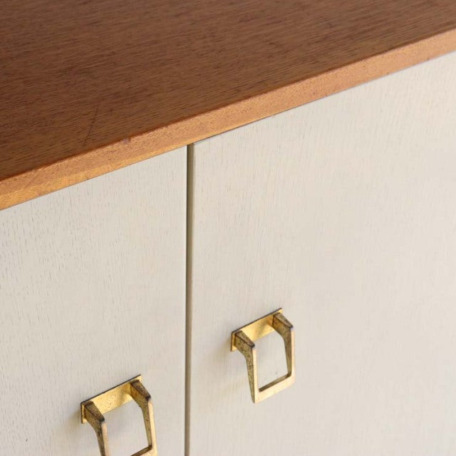 Mid-century British G-PLAN teak cabinet with cream doors, brass geometric handles, and visible wood grain edges.