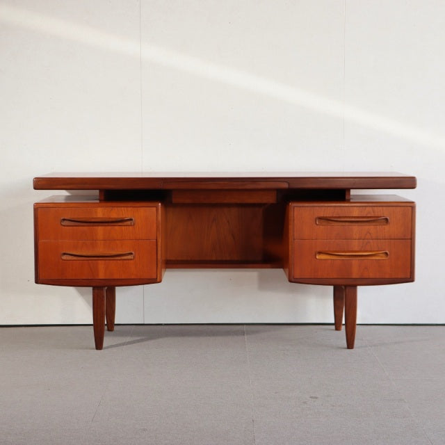 Mid-century British G-Plan vintage teak desk with sleek wood grain, tapered legs, and four rounded drawer fronts.