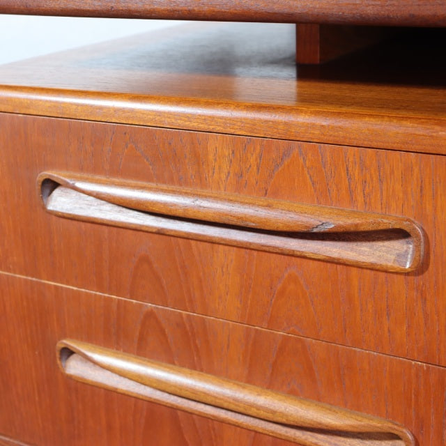 Close-up of vintage British mid-century teak desk drawers with smooth wood grain and integrated curved handles.